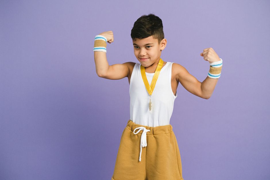 Photo by Anna Shvets on Pexels Young boy confidently flexes muscles with medal and sportswear. Perfect for themes of achievement and confidence. - Photo by Anna Shvets on Pexels