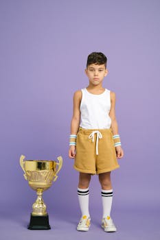 Child standing next to a large trophy in a studio with a purple backdrop.