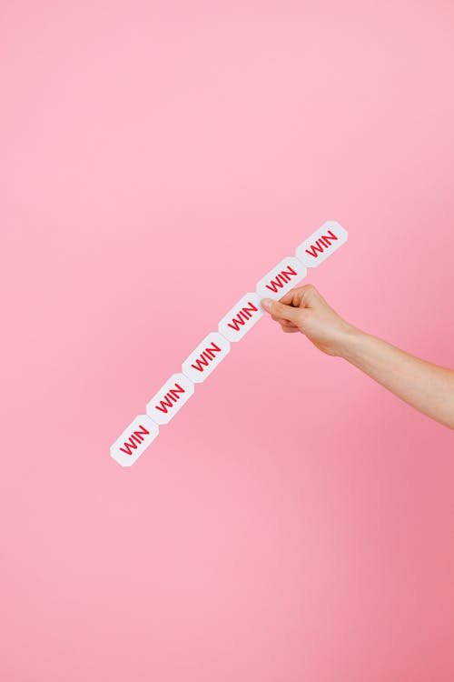 Hand Holding a Sign Saying "Win" on a Pink Background 