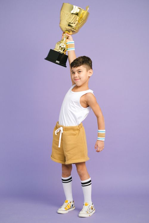 Free A cheerful young boy holding a large golden trophy, signifying victory. Stock Photo