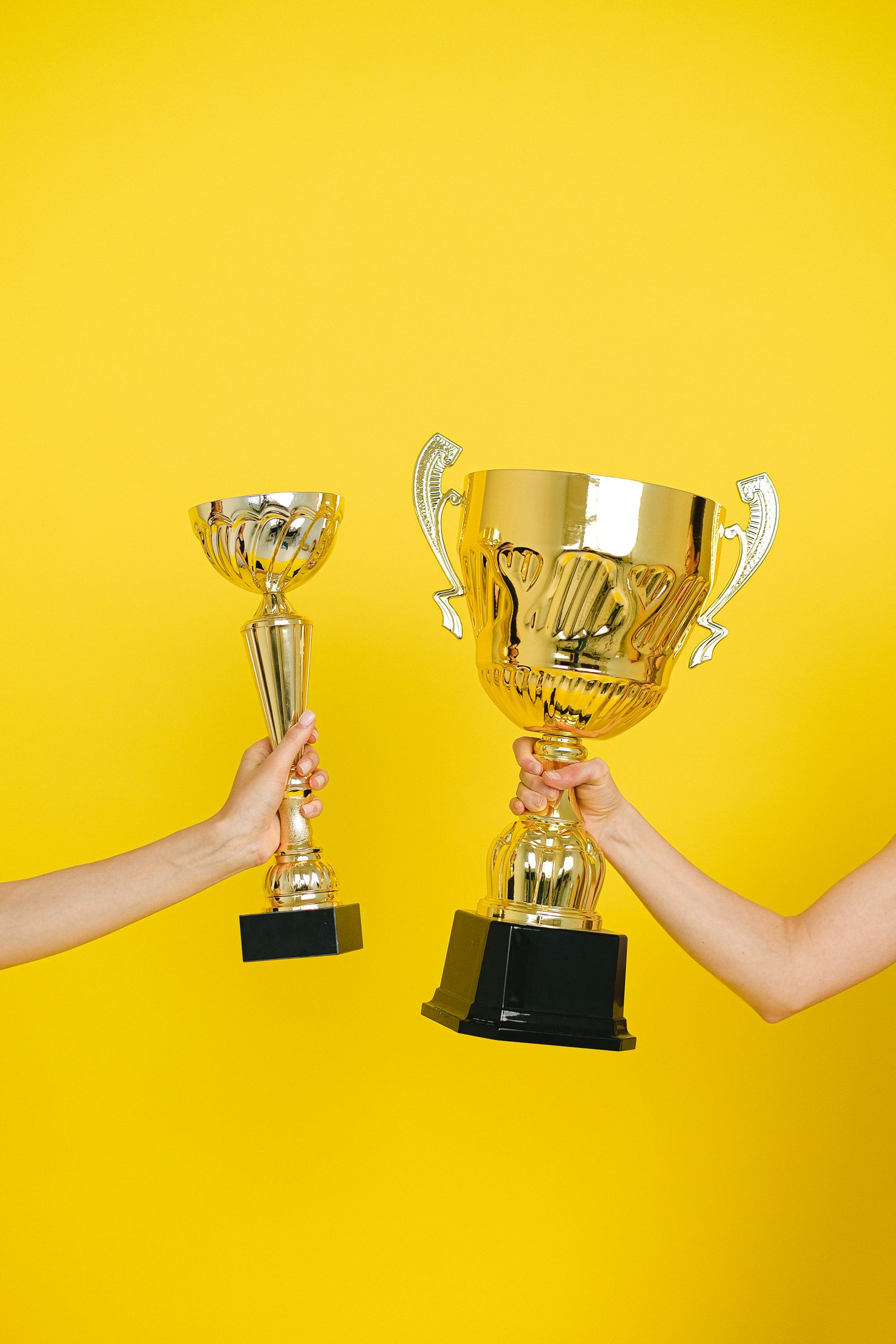 Two hands holding trophies against a vivid yellow backdrop