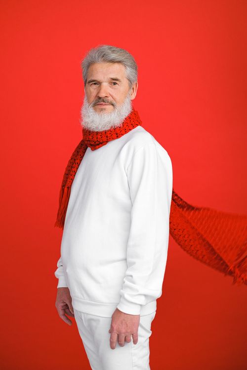 Free Elderly man in a white sweater with a red scarf against a bold red background. Stock Photo