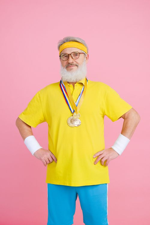 Free Elderly man in activewear proudly displays medals on a pink studio backdrop. Stock Photo