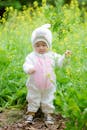 Baby in White Hoodie Standing on Green Grass Field