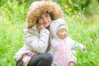 Woman in Beige and Brown Fur Jacket Sitting beside a Baby in White Hoodie Jacket