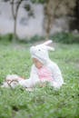 Baby in White Long Sleeve Hoodie Onesie Sitting on Green Grass Field