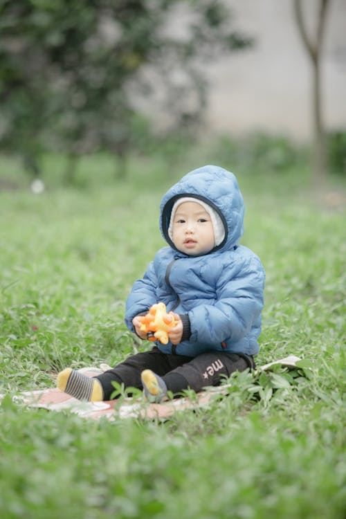 An Adorable Child in Winter Jacket Sitting on the Grass