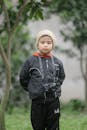 A Boy in Black Jacket Standing Near a Tree