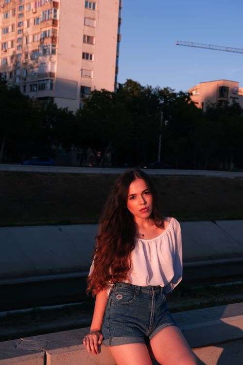 Free A young woman enjoys a warm sunset outdoors wearing denim shorts and a white top. Stock Photo