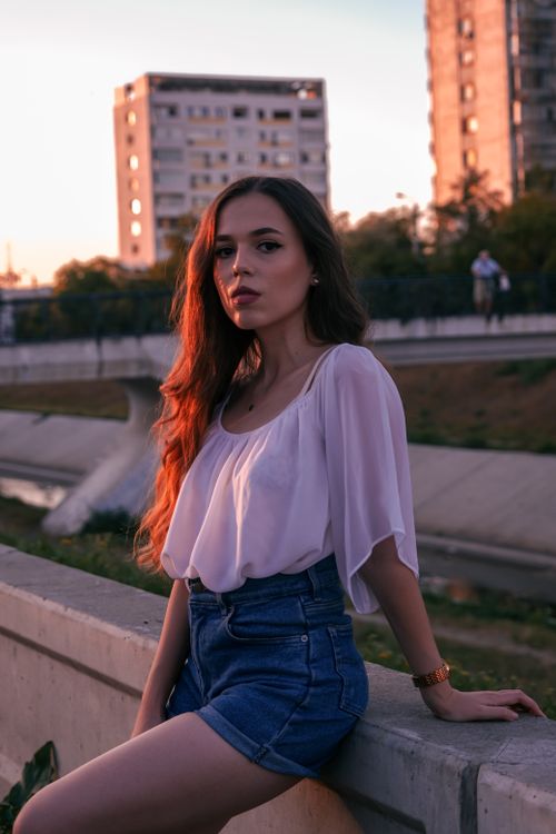 Free Young woman wearing denim shorts and white top posing by a canal at sunset. Stock Photo