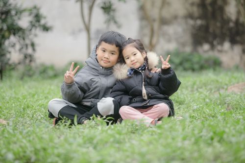 Free Two children sitting on grass, smiling and showing peace signs in winter wear. Stock Photo