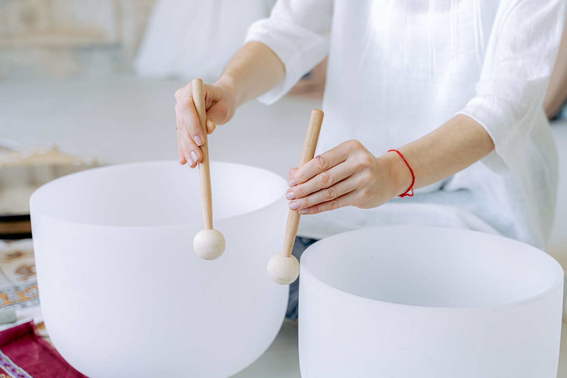 Hands playing crystal singing bowls with mallets, highlighting sound healing practice indoors.