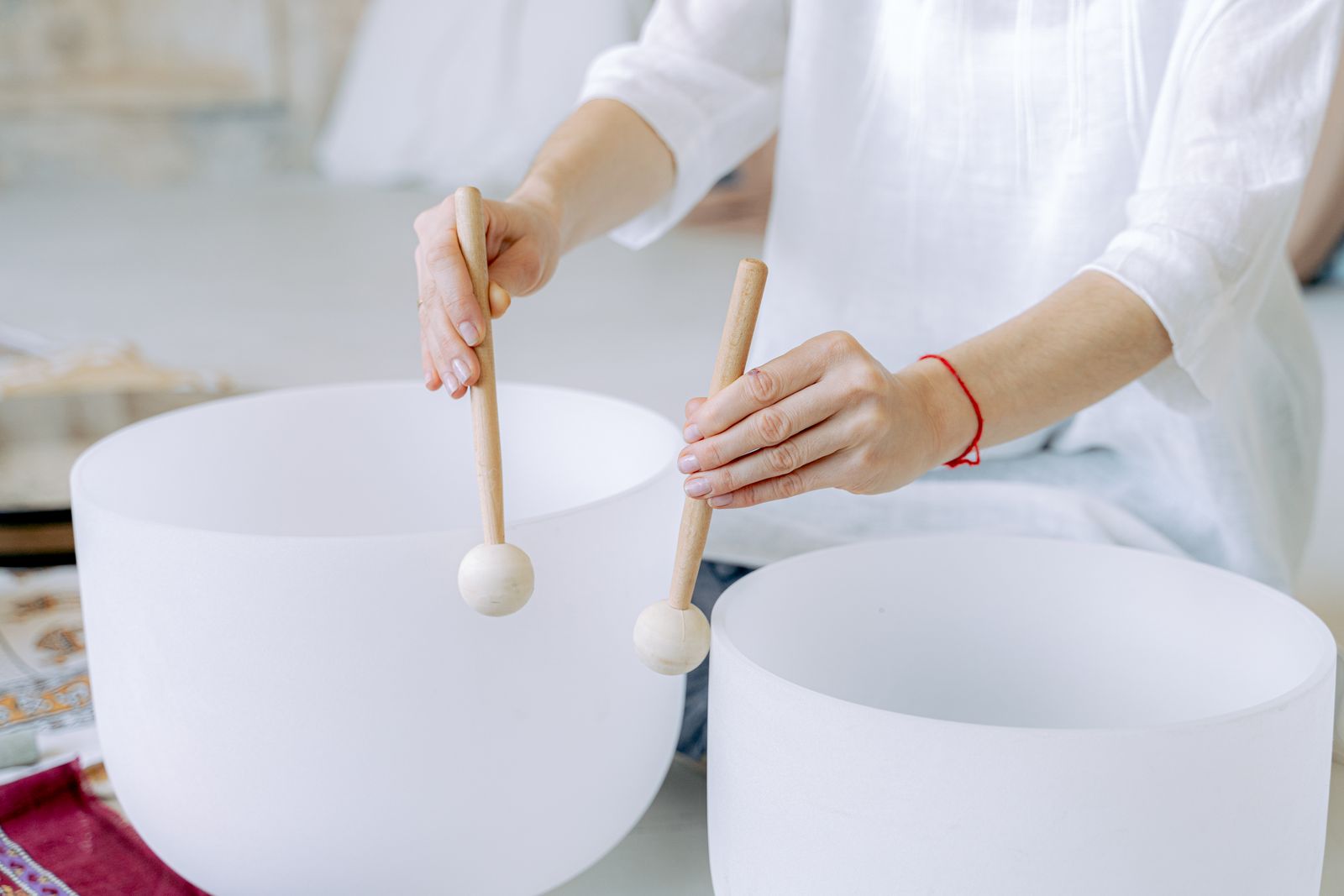 Hands playing white crystal singing bowls with felt mallets