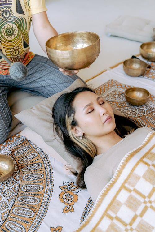 Free Photo of a Woman Lying Near a Person Playing a Tibetan Singing Bowl Stock Photo