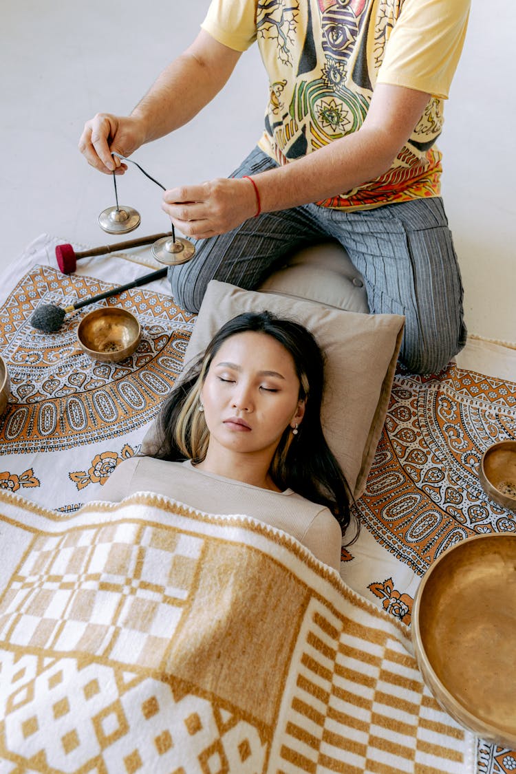 Photo Of A Woman Lying Near A Person Playing Tibetan Bells