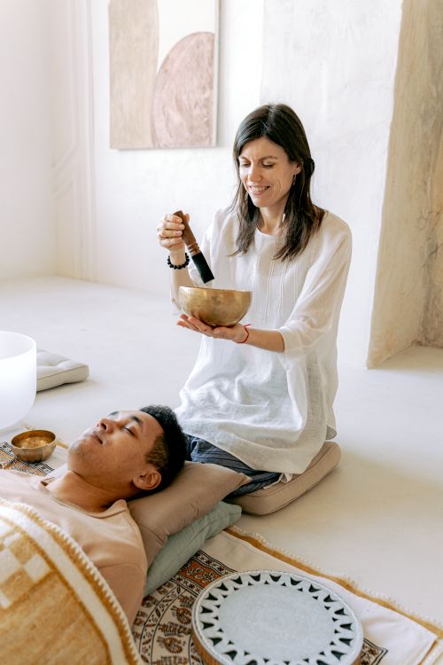 Free Woman performing sound healing with Tibetan singing bowl over man's head in serene indoor setting. Stock Photo