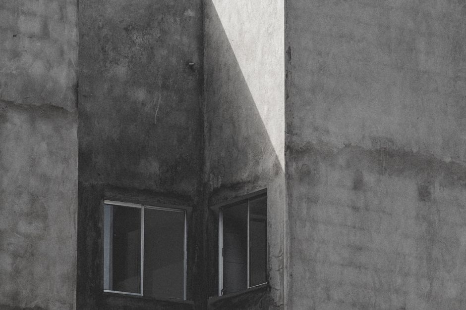 Weathered concrete residential facade with damp staining and open windows, evoking moisture ingress issues.