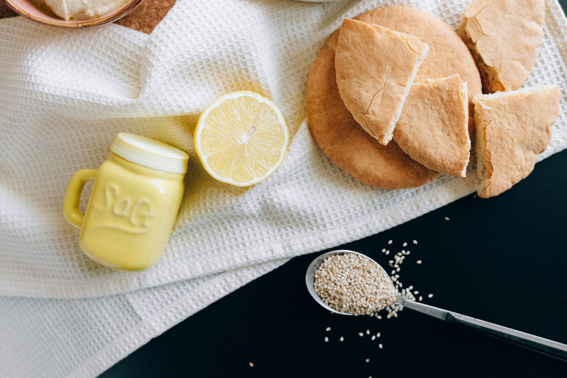A rustic breakfast arrangement featuring fresh bread, a sliced lemon, and sesame seeds.