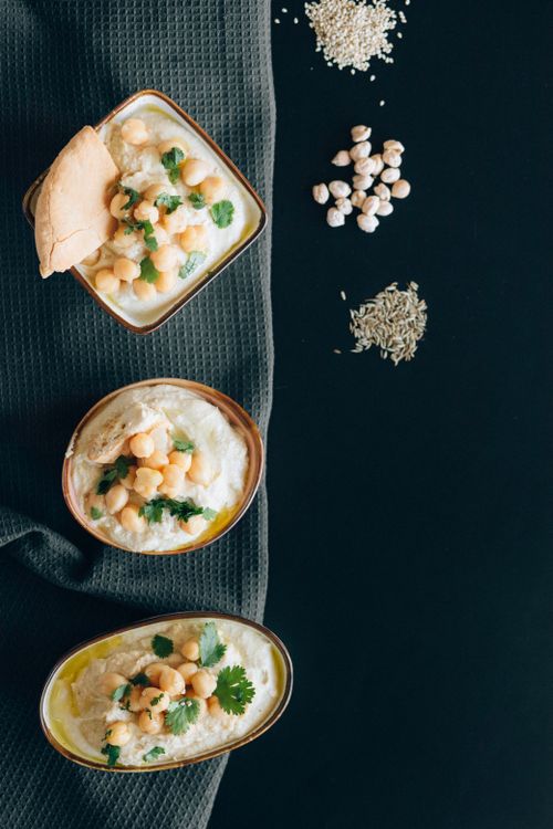 Free A top-down view of creamy hummus bowls garnished with fresh chickpeas and herbs displayed on a dark background. Stock Photo