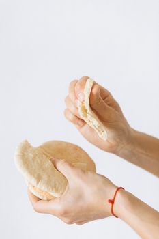 Close-up of hands breaking fresh pita bread against a white background.