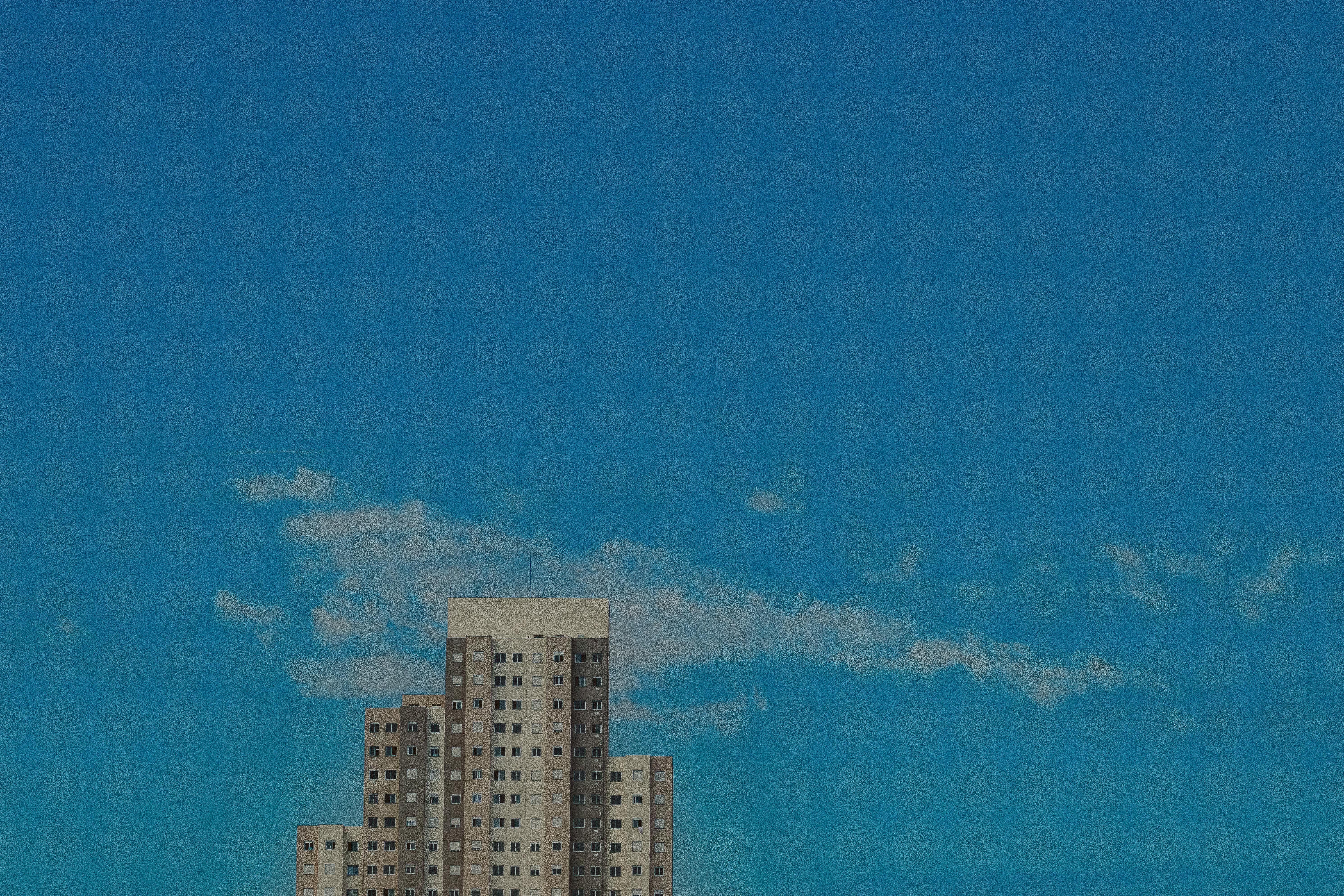 A tall residential building set against a clear blue sky with sparse clouds, showcasing urban architecture.