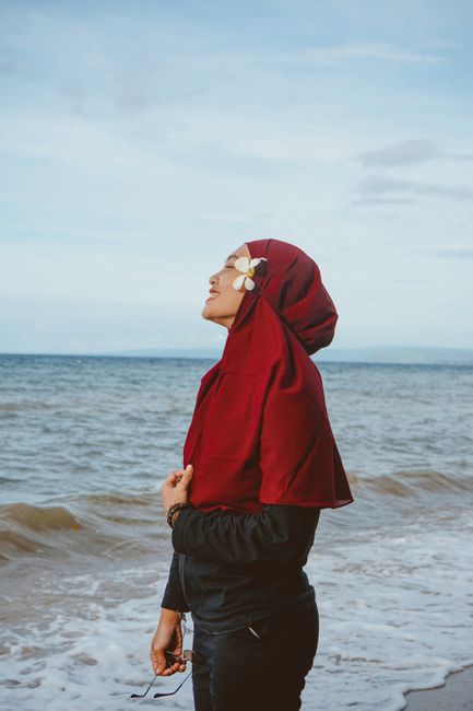 Side view of smiling Muslim female standing on beach washed by waving foaming sea during vacation
