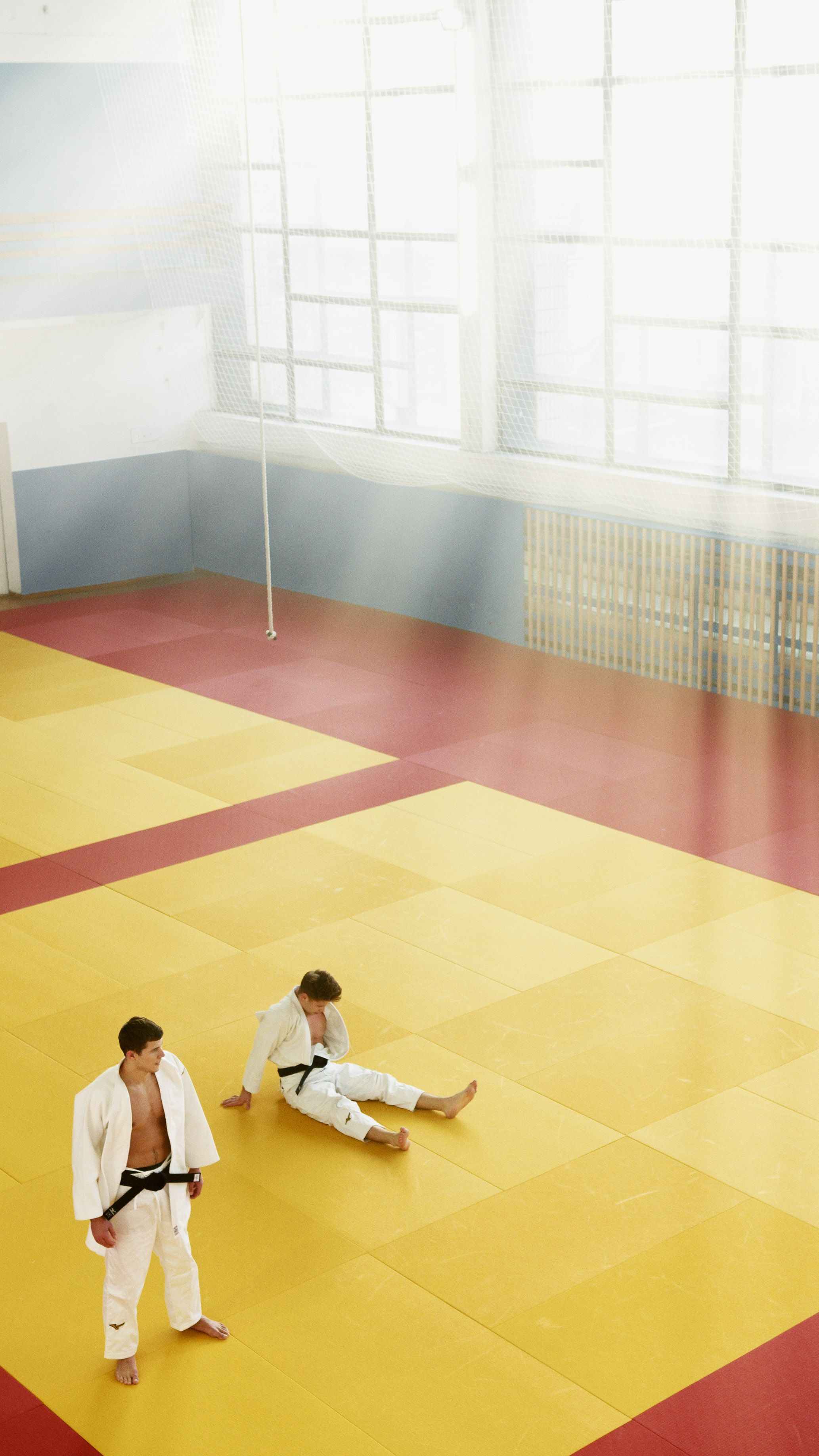 Two athletes practice judo in a sunlit dojo, wearing traditional uniforms.