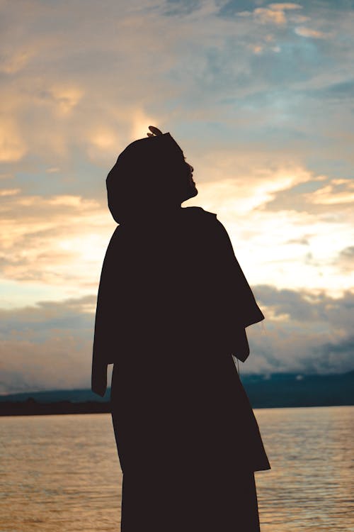 Silhouette of woman standing near sea at sunset