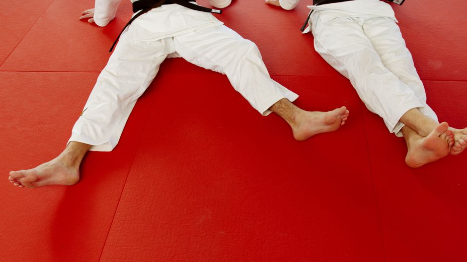 Two martial artists in white uniforms resting on a red training mat, showcasing physical endurance.