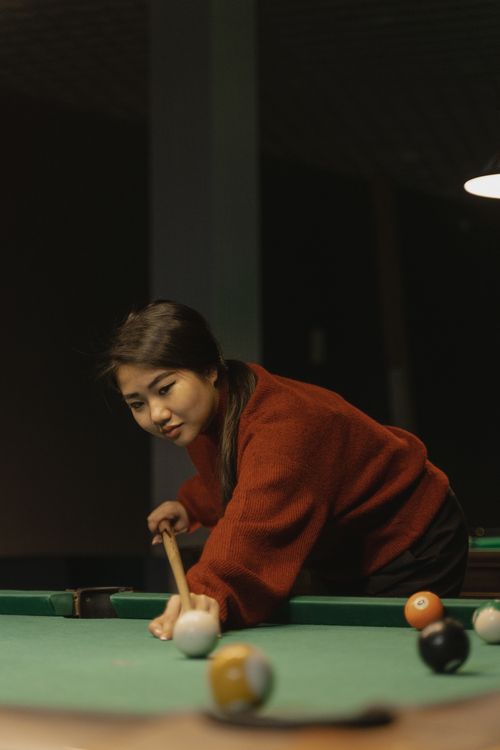 Free A woman focuses on taking a precise pool shot with a cue stick indoors, highlighting concentration and skill. Stock Photo