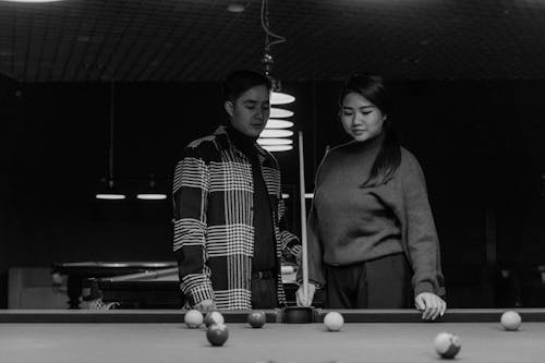 Grayscale Photo of a Man and a Woman Standing Near a Pool Table