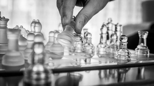 Grayscale Photo of a Person's Hand Playing Chess