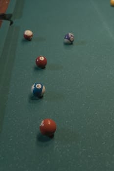 Top view of billiard balls scattered on a classic green table, displaying a vertical alignment.