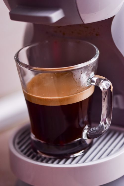 Free Glass mug with freshly brewed americano placed on cup holder of coffeemaker in light kitchen with modern equipment at home Stock Photo
