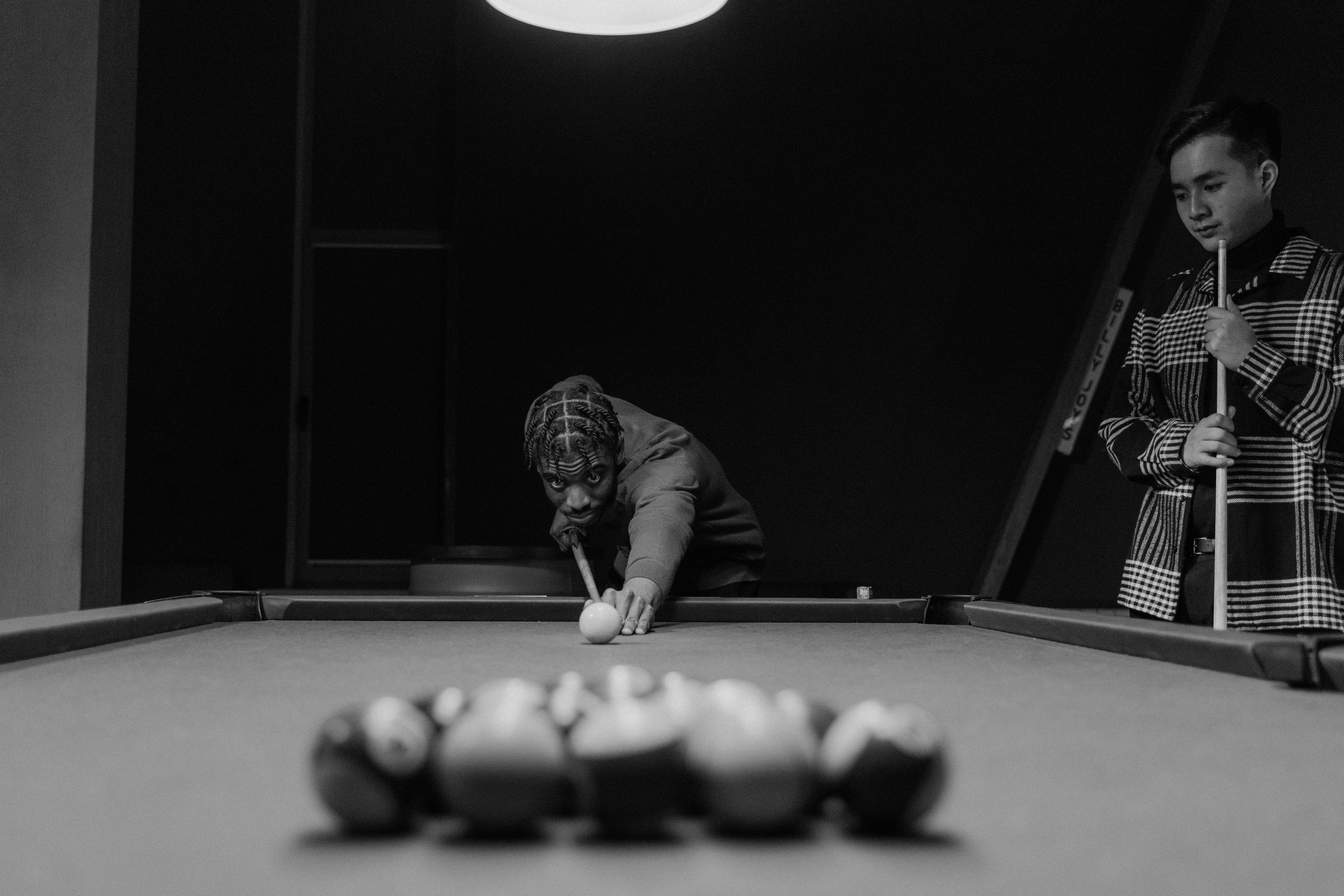 Engaging black and white billiards scene with players in action, highlighting focus and precision.