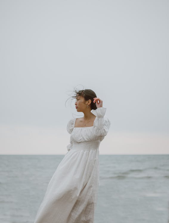 Gentle Asian traveler in white dress contemplating sea