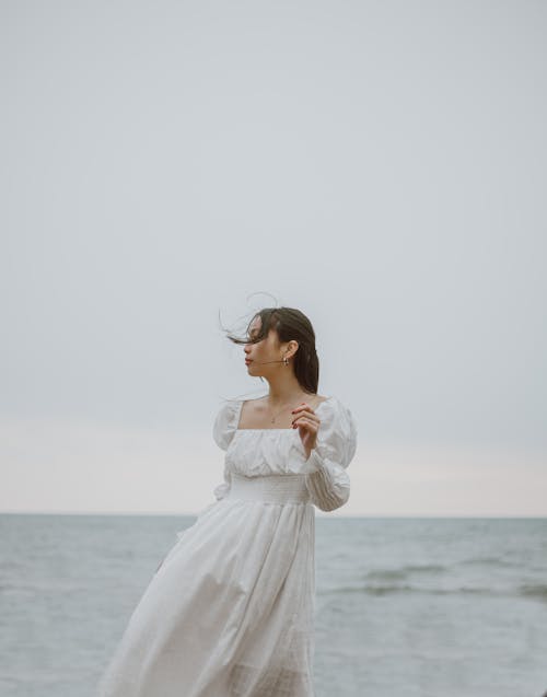 海岸に立っている白い長袖のドレスの女性