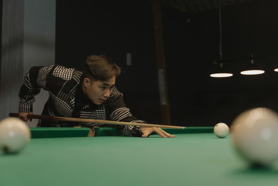 Young man aiming a cue in a billiards game under dim lighting. Young man aiming a cue in a billiards game under dim lighting.