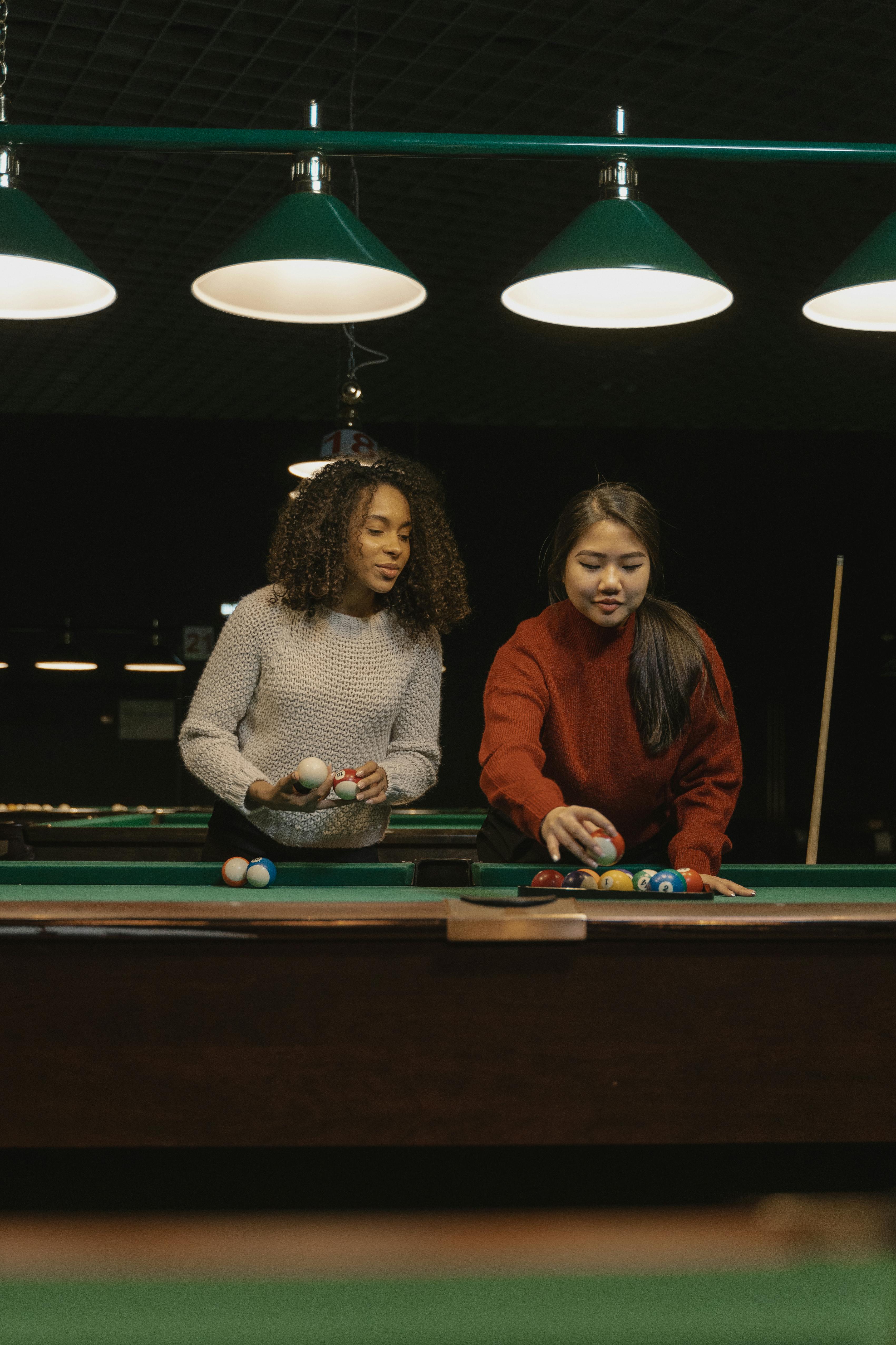 Two young women play billiards indoors, enjoying leisure time together.