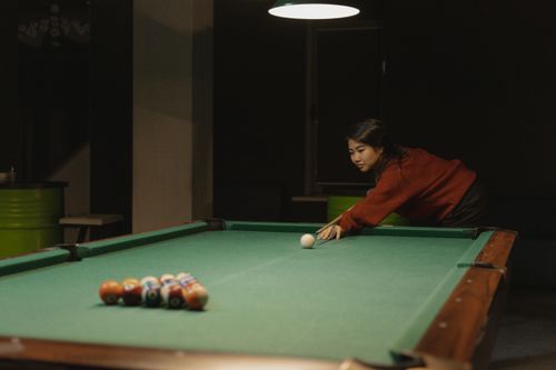 Free A young woman concentrates as she plays pool in a dimly lit room, showcasing leisure and focus. Stock Photo