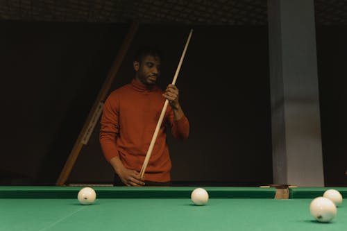 A Man in Orange Long Sleeves Looking at The Cue Stick He's Holding