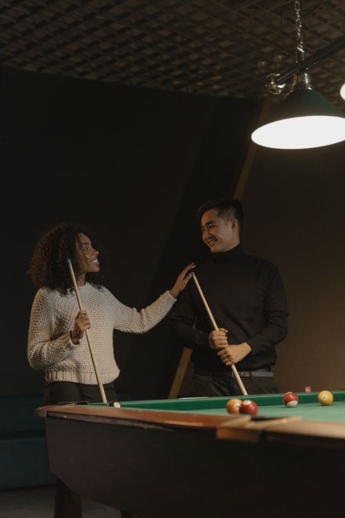 Free A man and woman smiling while playing billiards together indoors, holding cue sticks. Stock Photo
