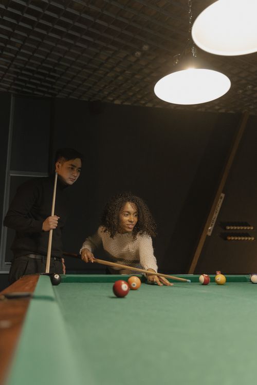 Free Two friends enjoying a casual billiards game indoors, focusing on a strategic shot. Stock Photo