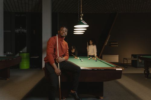 Free Group playing billiards in a modern pool hall, with focus on a man holding a cue stick. Stock Photo