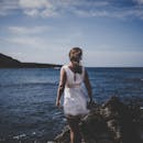 一名身穿白色连衣裙的女子在美丽的夏日日落中，于岩石海滩上享受时光