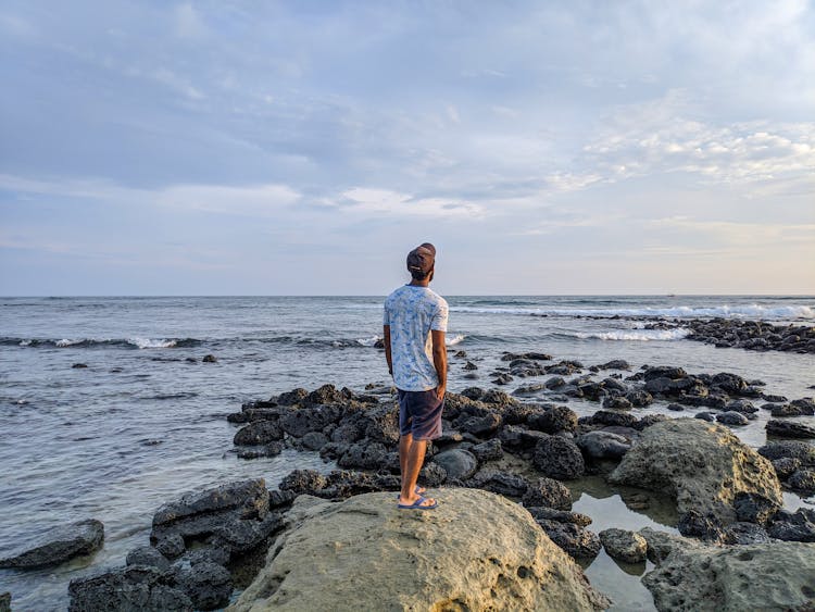 A Man Standing On A Big Rock Near The Sea