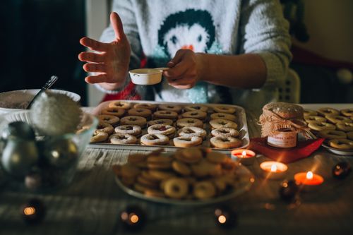 Free Hands preparing festive cookies with powdered sugar in a cozy holiday setting. Stock Photo