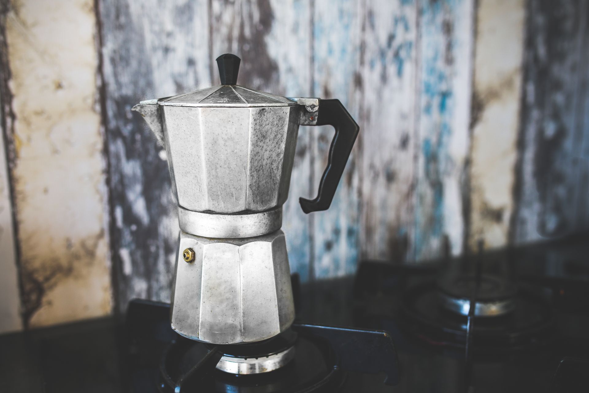A vintage moka pot brewing on a gas stove with a rustic wooden background, perfect for coffee lovers.
