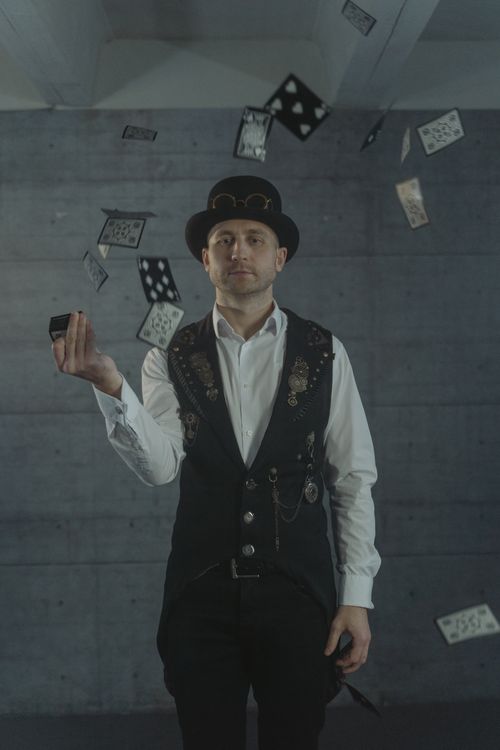 Free Magician in a hat performing a card trick indoors with cards mid-air. Stock Photo