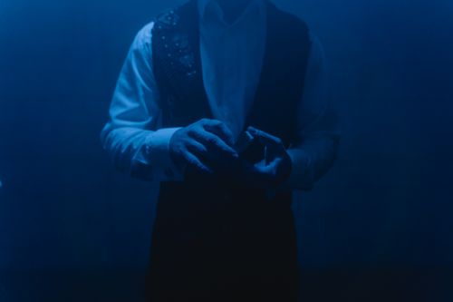 Free Magician in a dark room skillfully performing a card trick under blue lighting. Stock Photo